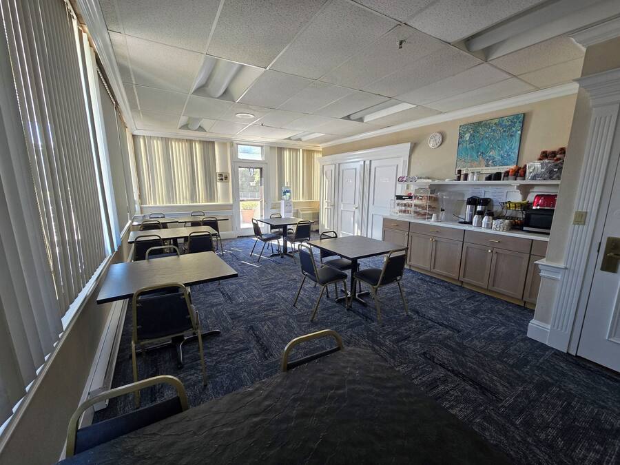 A hotel room with a dining area, a kitchen, and a large window with blinds.