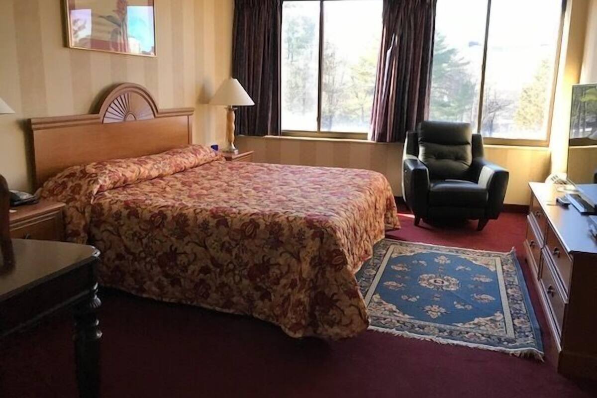 A hotel room with a large bed, a desk, a chair, and a window with curtains.