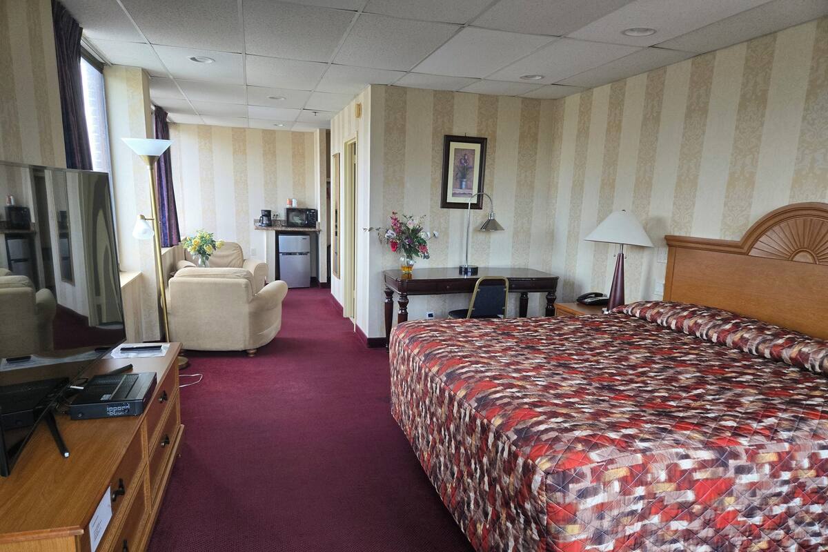 A hotel room with a bed, a desk, a chair, a TV, and a kitchenette.