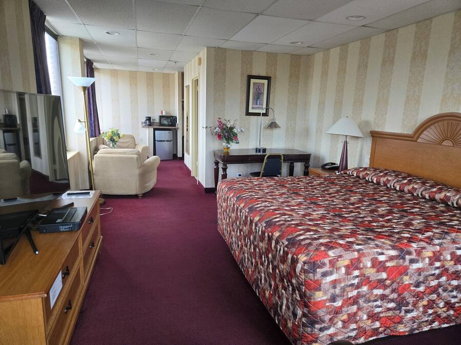 A hotel room with a bed, a desk, a chair, a TV, and a kitchenette.