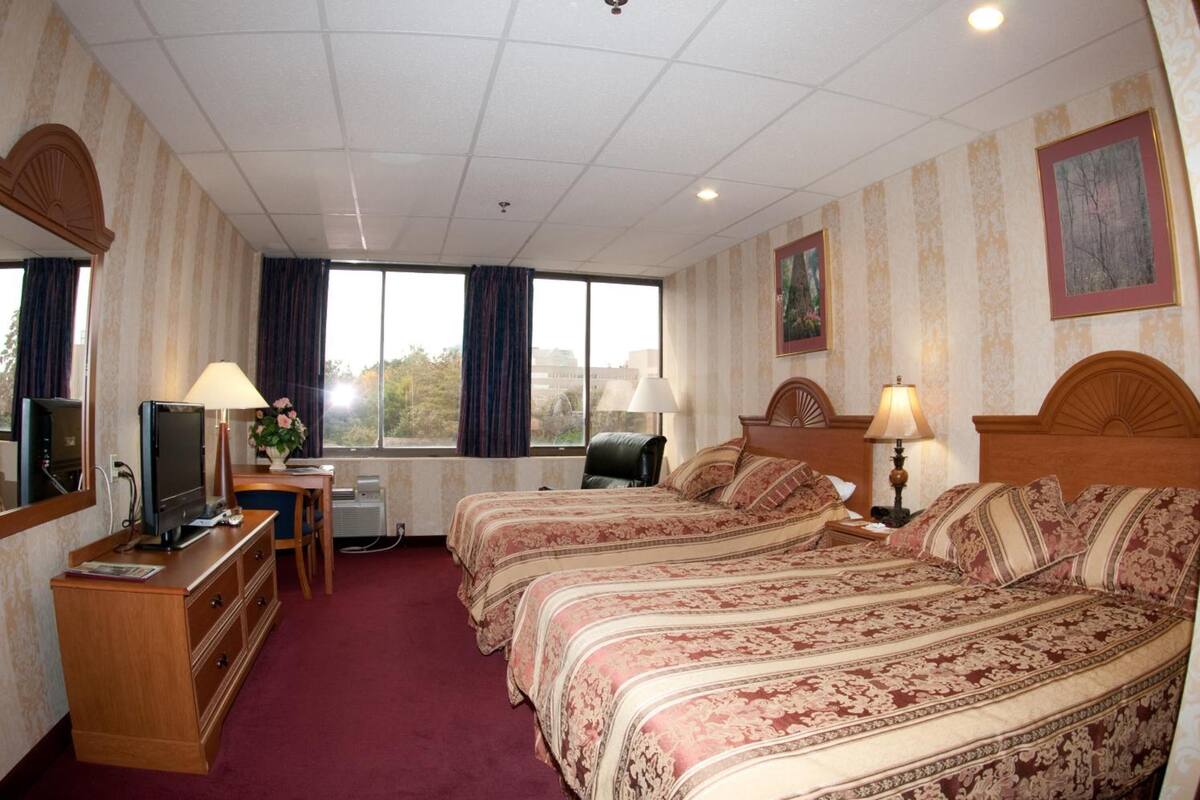 A hotel room with two beds, a desk with a computer, a TV, and a window with curtains.