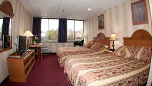 A hotel room with two beds, a desk with a computer, a TV, and a window with curtains. - Amsterdam Hotel (Stamford)