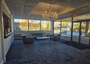 Un hall d’entrée agrémenté d’un lustre, d’un espace salon et de grandes fenêtres donnant sur la rue.