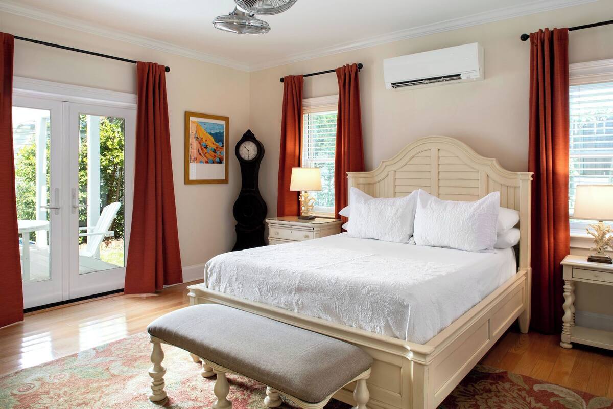 A bedroom with a large bed, a bench, a clock, and an air conditioning unit.