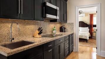 Una cocina moderna con muebles oscuros, un microondas de acero inoxidable, un lavamanos y un bloque para cuchillos.