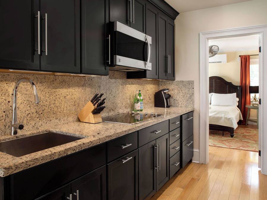Una cocina moderna con muebles oscuros, un microondas de acero inoxidable, un lavamanos y un bloque para cuchillos.