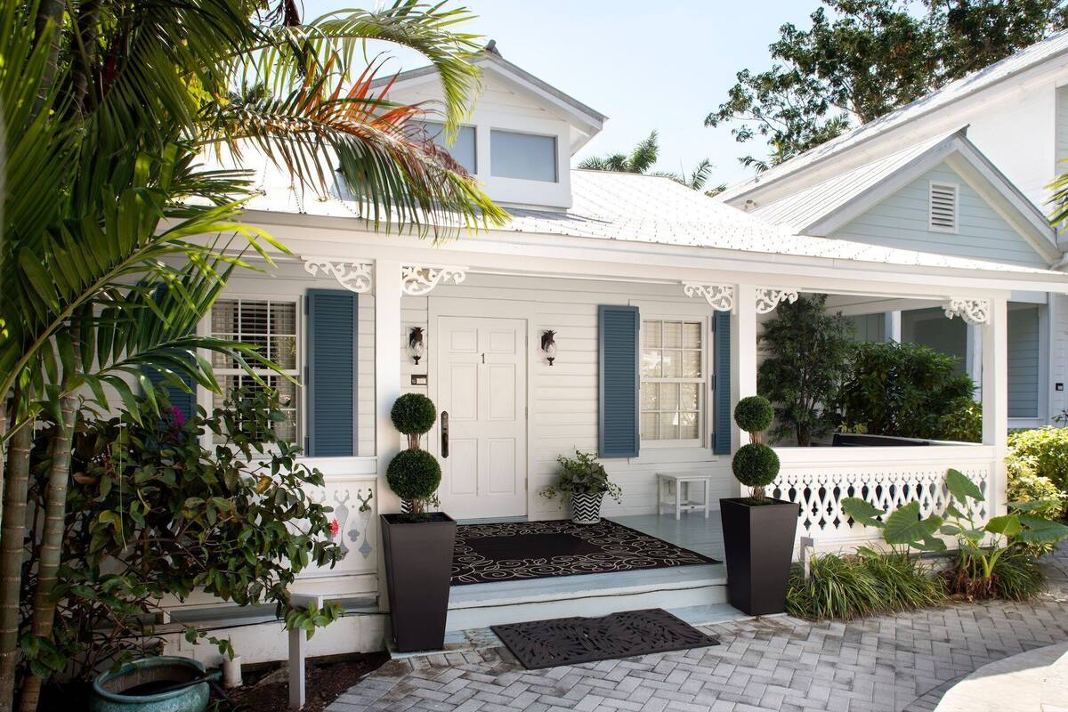 A white house with blue shutters, a front porch, and potted plants.
