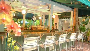 A bar area with a counter, chairs, and a clock. - The Gardens Hotel (Key West)