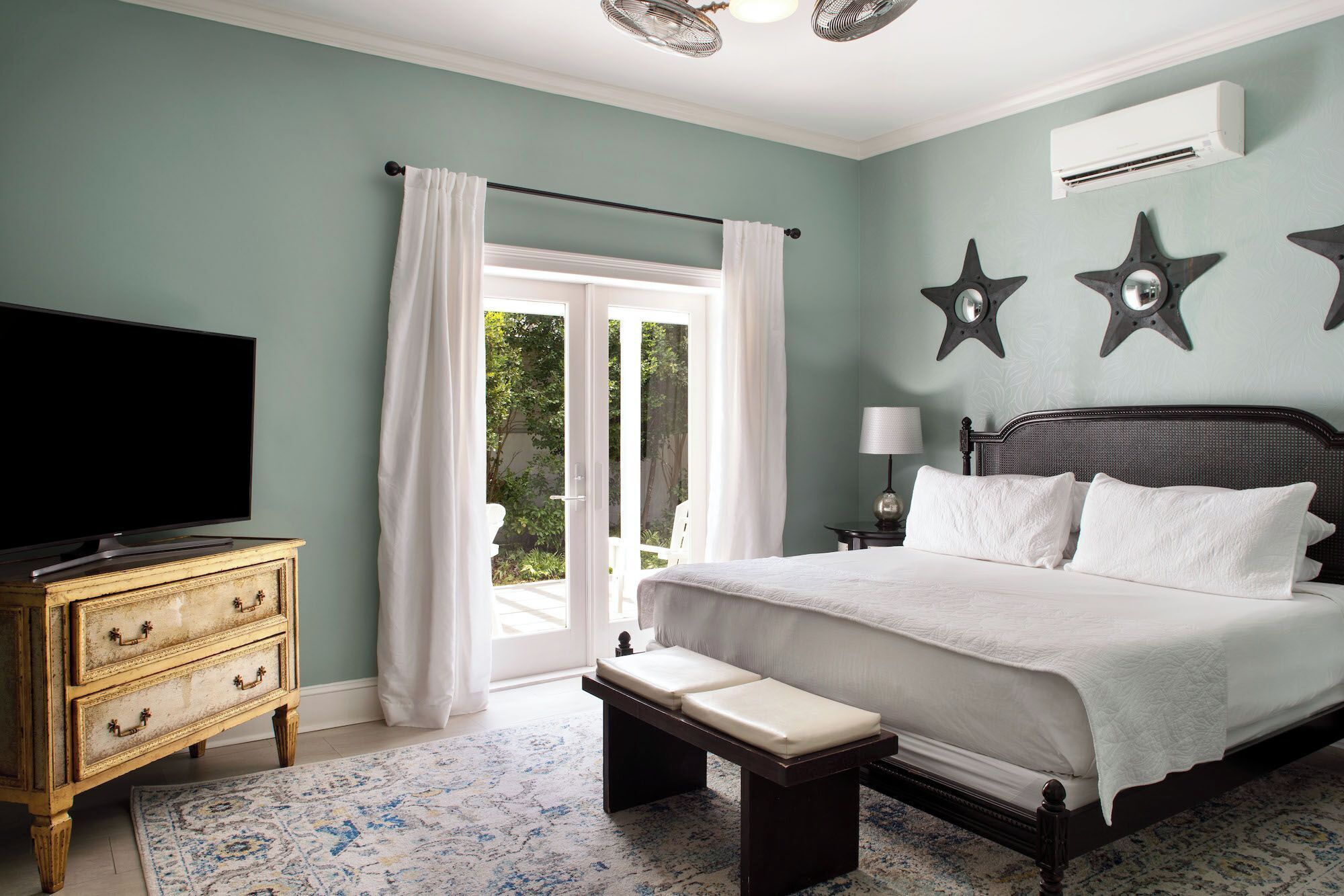 A bedroom with a bed, a bench, a dresser, a TV, and a window with curtains.