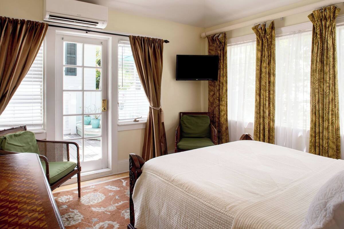 A hotel room with a bed, a chair, a television, and a window with curtains.