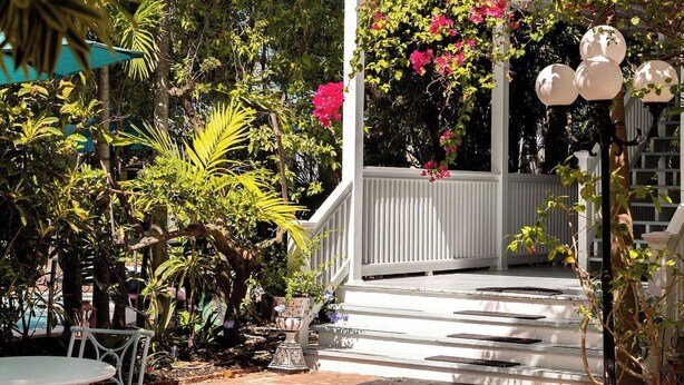 A garden pathway leading to a white gazebo with pink flowers, surrounded by lush greenery and a white fence. - The Gardens Hotel (Key West)