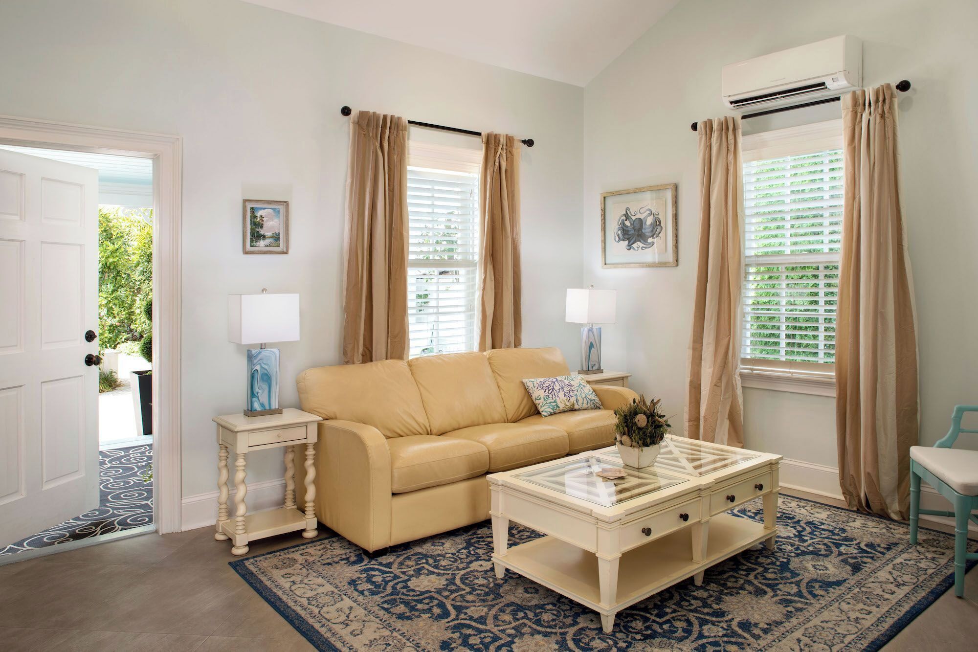 A living room with a beige sofa, a glass coffee table, a patterned rug, and two side tables with lamps.