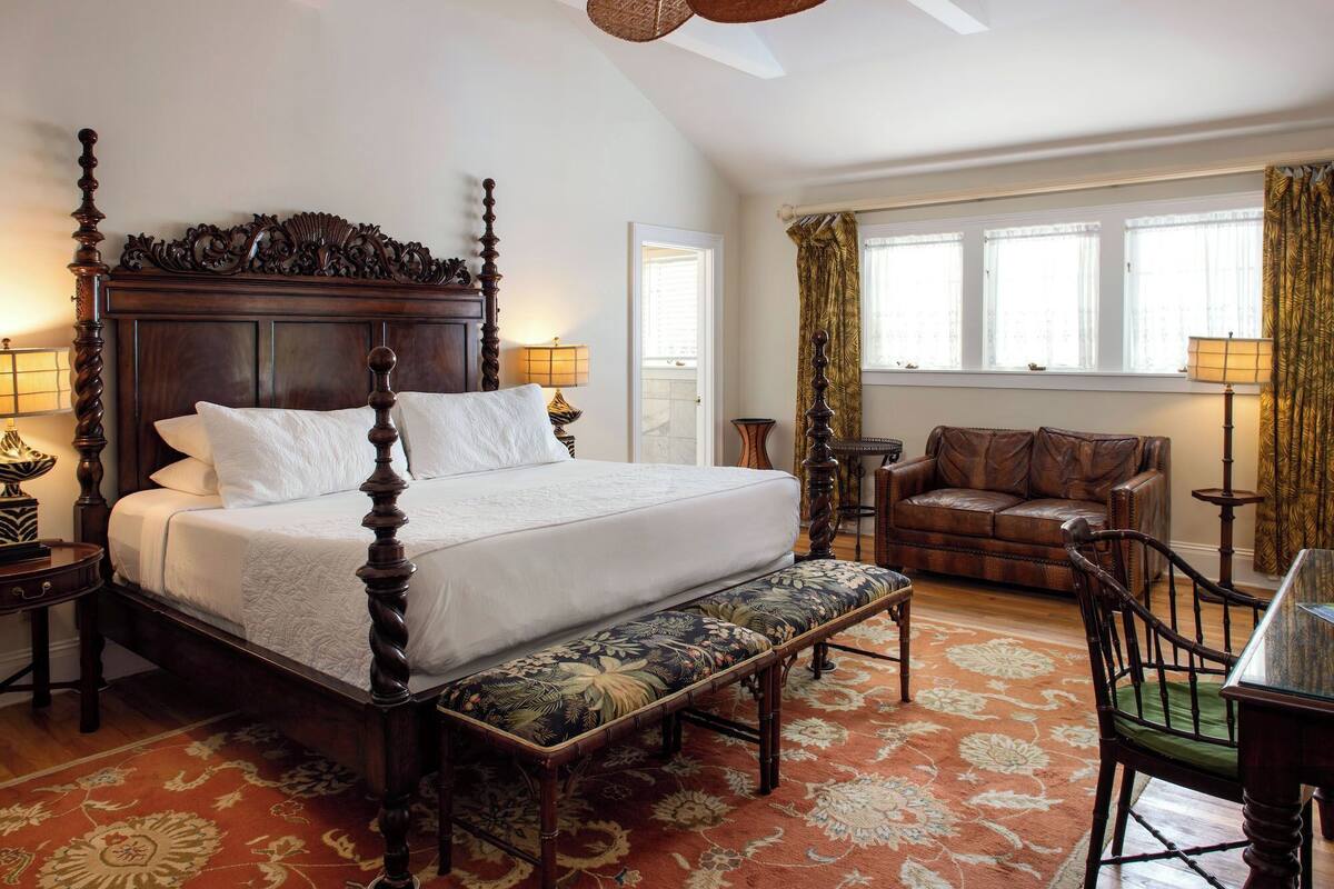 A bedroom with a four-poster bed, a bench, a leather sofa, and a dining table.