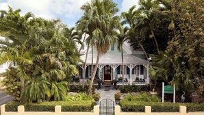 A colonial-style building with a porch, surrounded by lush tropical vegetation. - The Gardens Hotel (Key West)