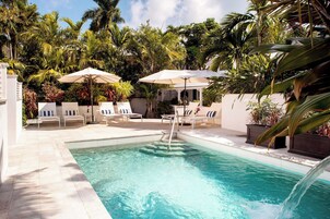 Un área de piscina con sillas de descanso y sombrillas, rodeada de plantas tropicales.