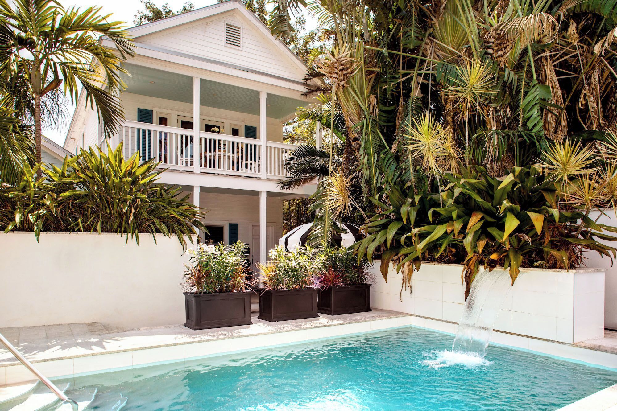 A pool area with a white building, a balcony, and various tropical plants.