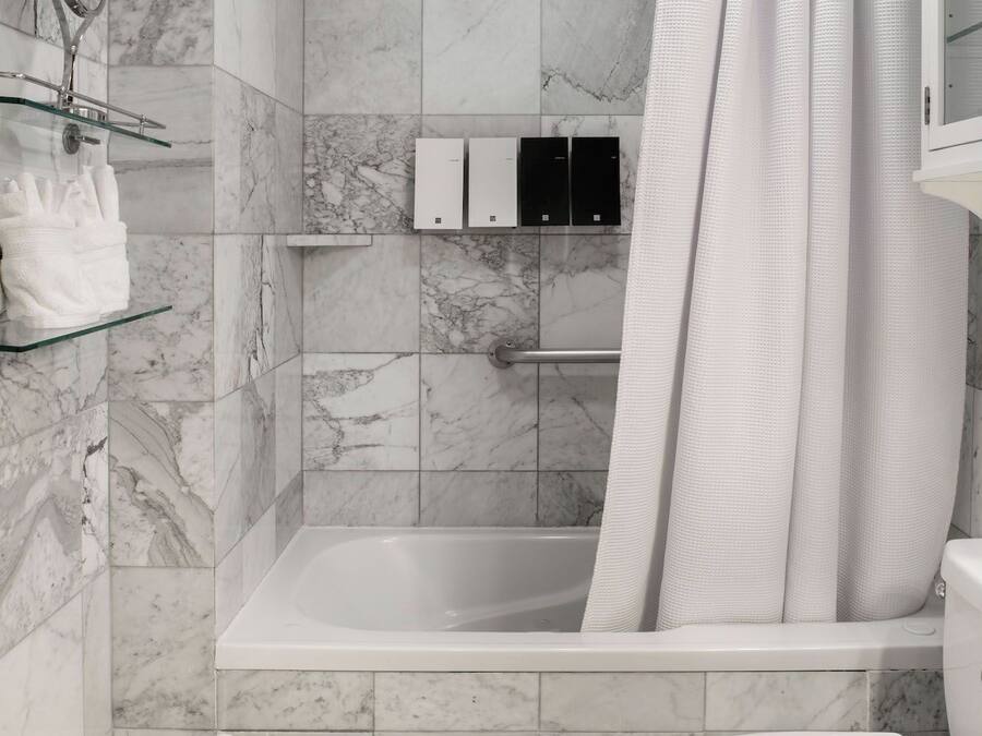 A modern bathroom with a marble-tiled shower, a glass shelf with toiletries, a toilet, and a basket of towels.