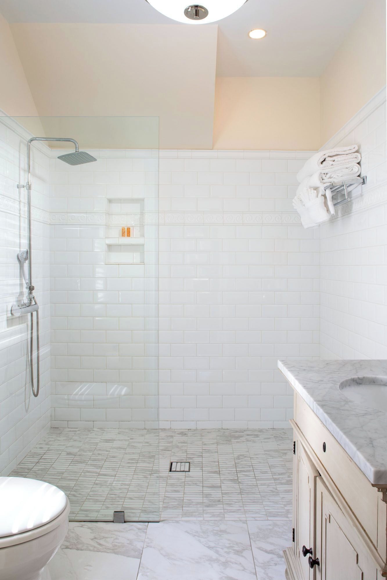 Un baño moderno con azulejos blancos tipo metro, ducha con cerramiento de vidrio, suelo de mármol e lavamanos con encimera de mármol.