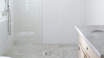 Un baño moderno con azulejos blancos tipo metro, ducha con cerramiento de vidrio, suelo de mármol e lavamanos con encimera de mármol.