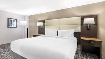 A hotel room with a large bed, two bedside tables with lamps, a framed picture on the wall, and a carpeted floor.