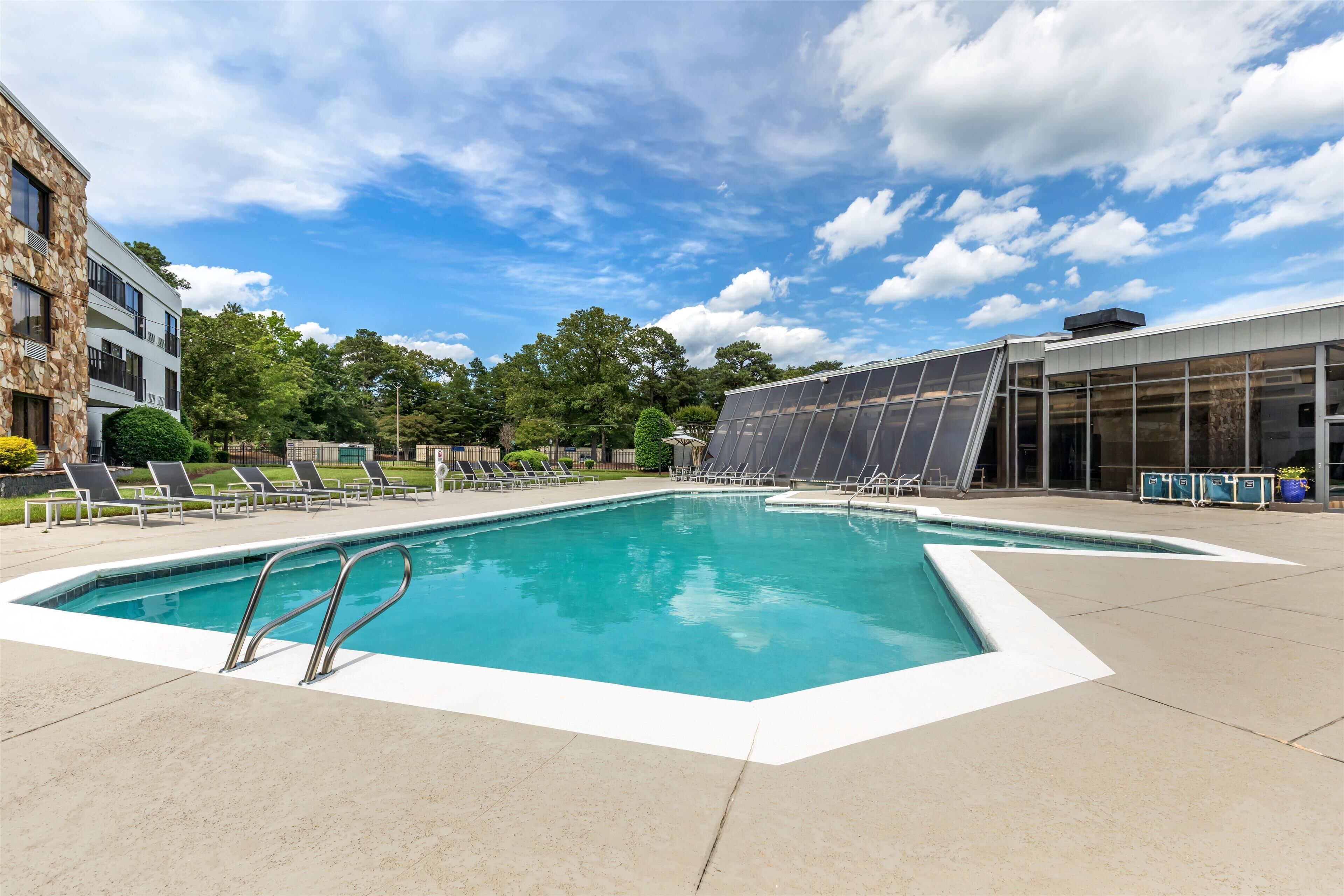 Una piscina con sillones de descanso y un edificio moderno con grandes ventanales.