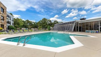 Una piscina con sillones de descanso y un edificio moderno con grandes ventanales.