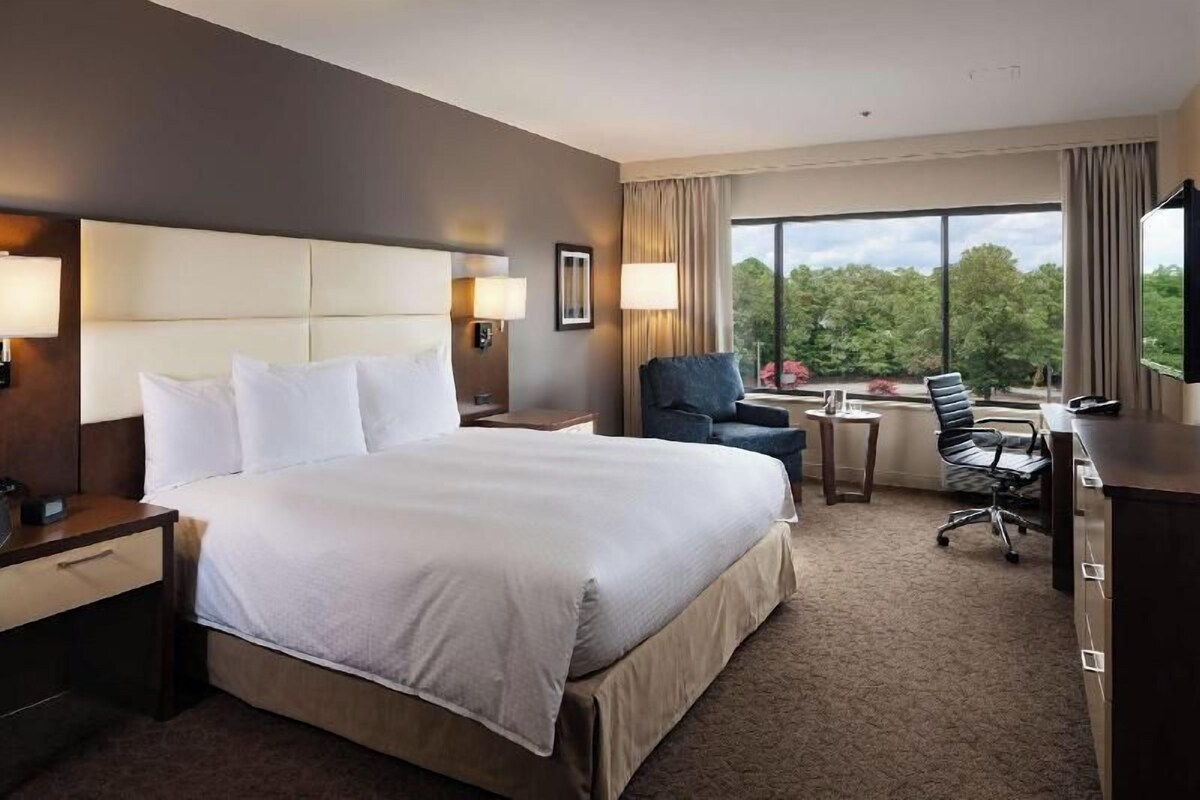 A hotel room with a large bed, a desk, a chair, and a view of the outdoors.