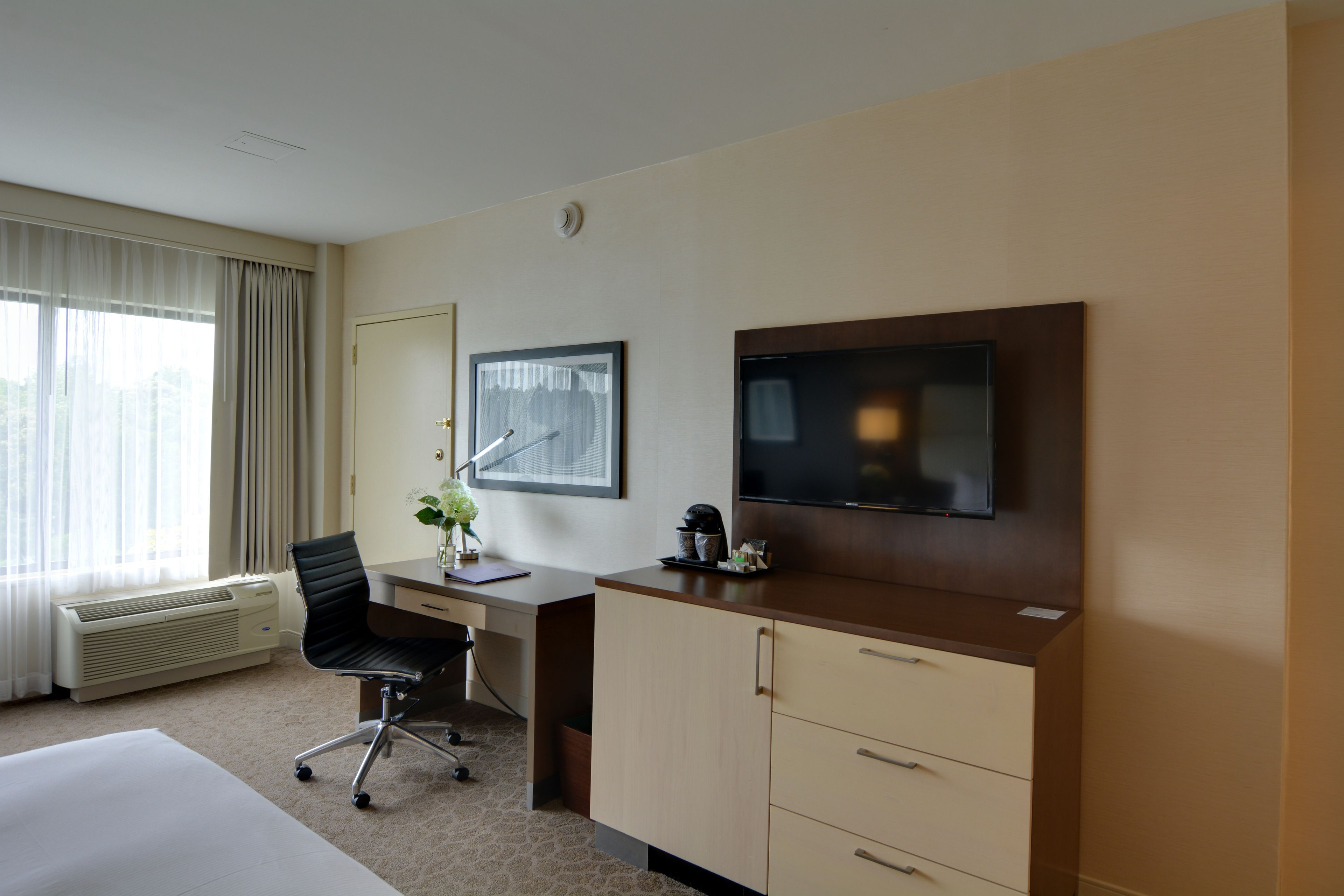A hotel room with a bed, a desk, a chair, a television, and a window with curtains.