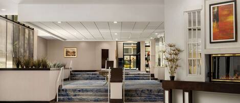 A modern hotel lobby with a central staircase, a fireplace, and a large painting on the wall.
