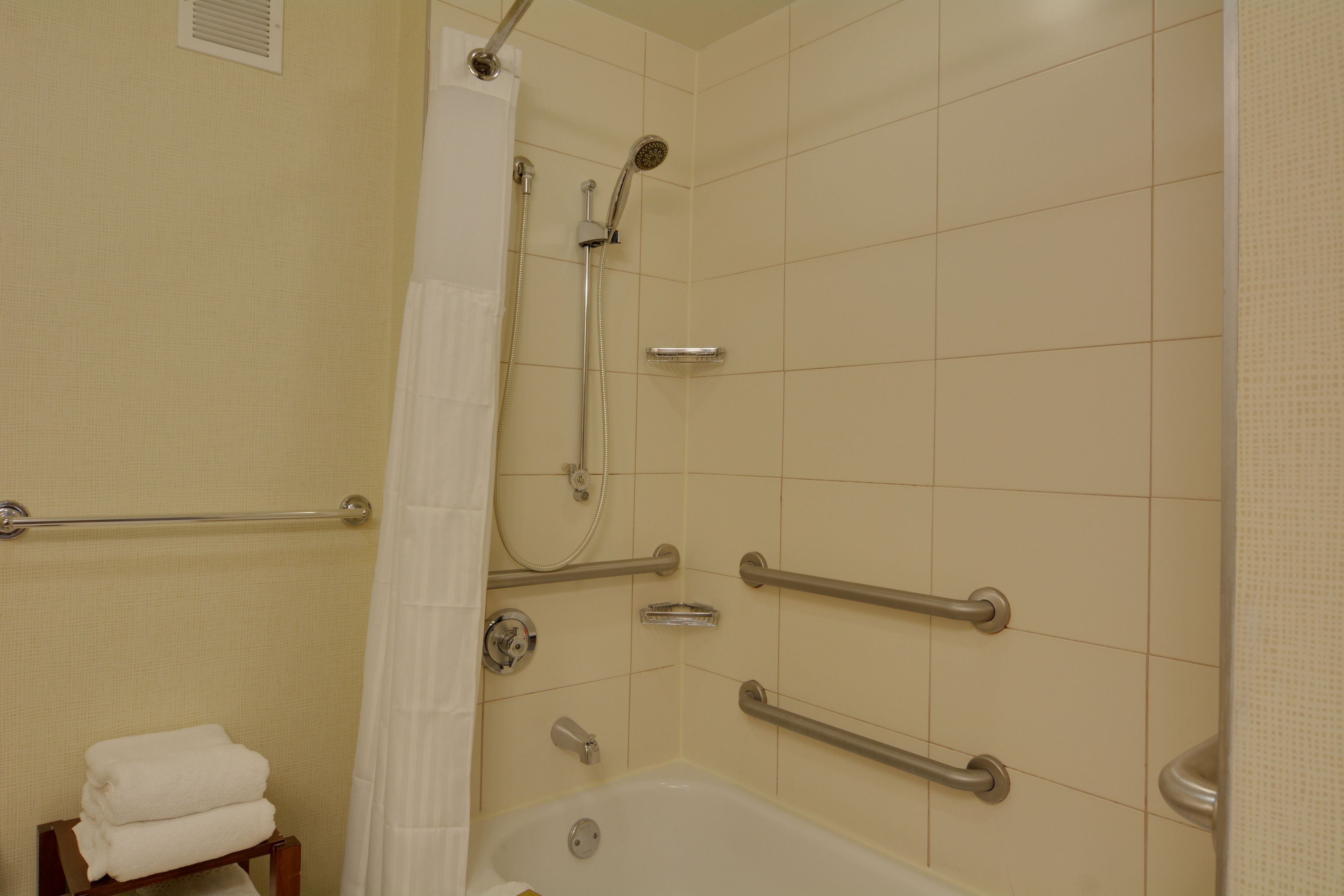 Une salle de bain équipée d’une douche, de barres d’appui, d’un porte-serviettes et d’une baignoire.