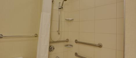 Une salle de bain équipée d’une douche, de barres d’appui, d’un porte-serviettes et d’une baignoire.