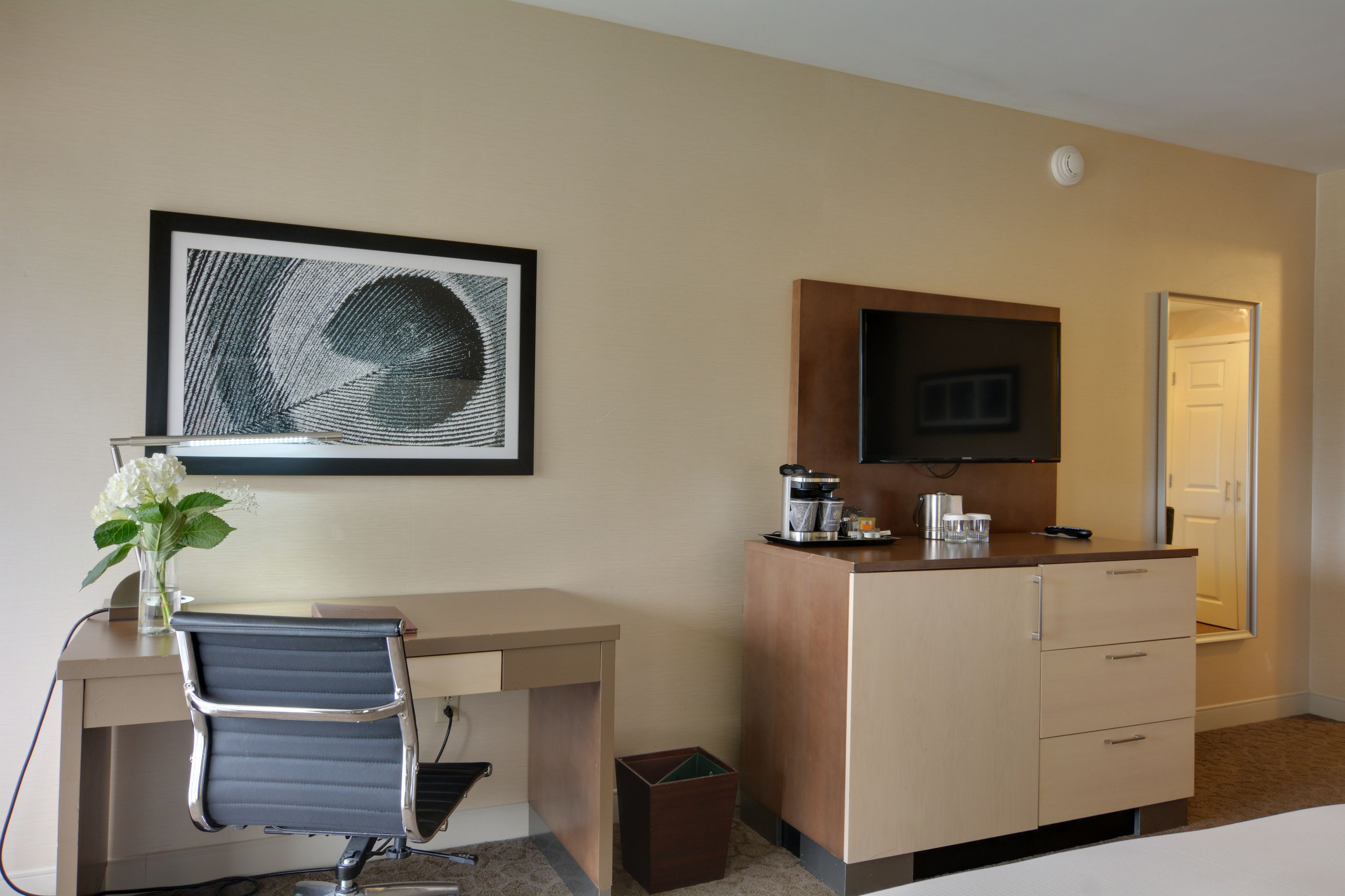 Habitación de hotel con escritorio, silla, televisor, minibar y una obra de arte enmarcada en la pared.
