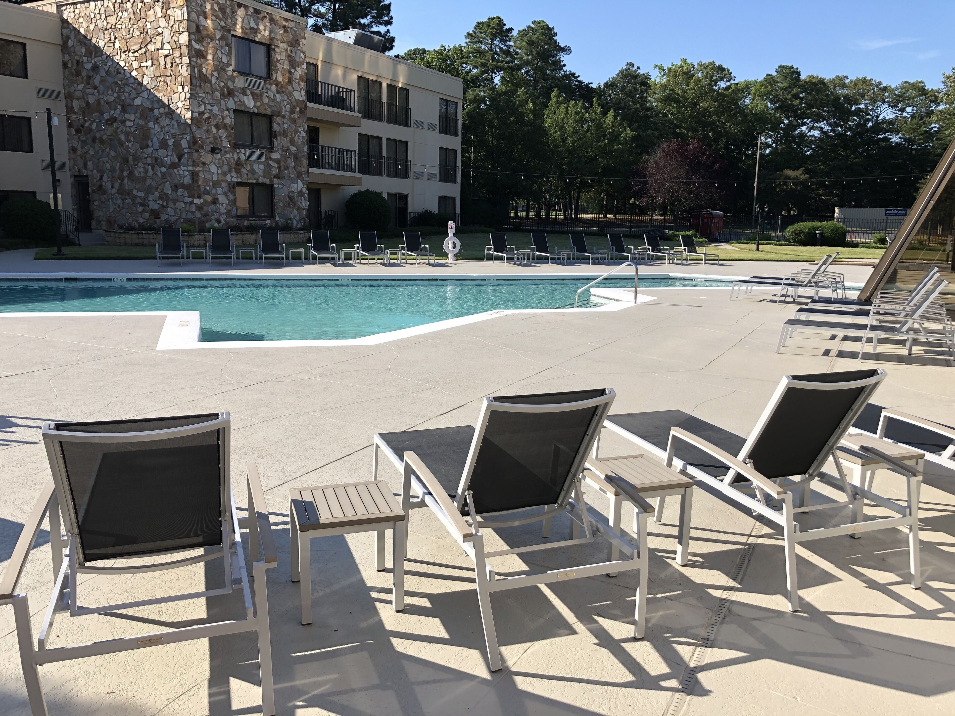 Zona de piscina con sillones de descanso y un edificio de piedra al fondo.