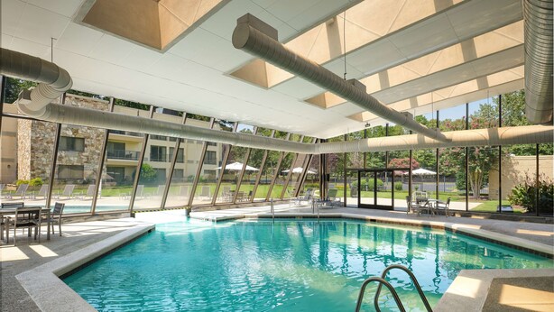 An indoor swimming pool with clear blue water, lounge chairs, and a view of a stone building and greenery outside. - DoubleTree by Hilton Williamsburg (Williamsburg)