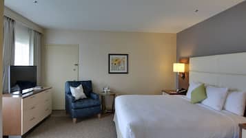 Habitación de hotel con cama, escritorio con televisor, una silla, mesita de noche y lámpara de pared.