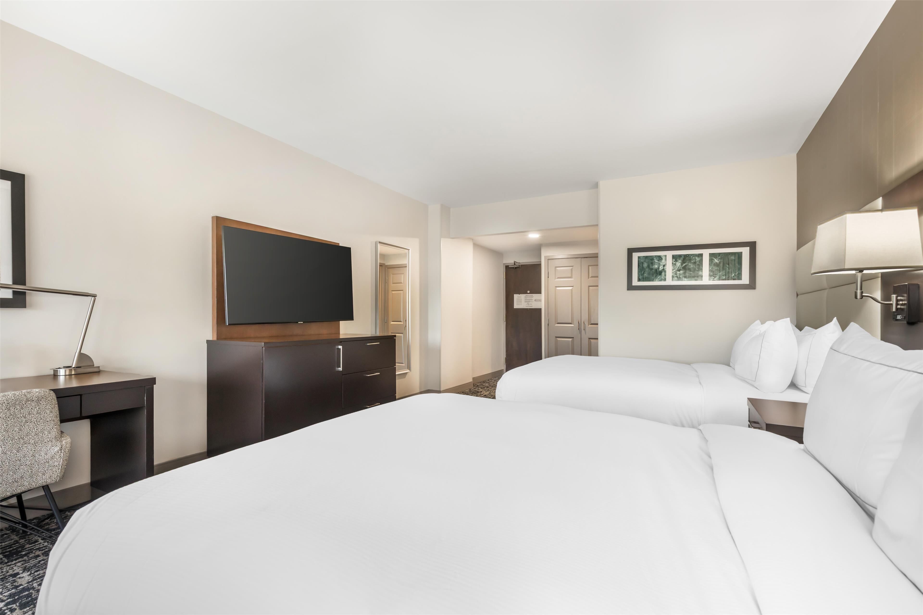 Ein Hotelzimmer mit einem großen Bett, einem Schreibtisch mit Stuhl, einem Fernseher und einem Kleiderschrank.