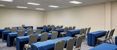 A conference room with rows of tables and chairs, equipped with ceiling lights and carpeted flooring.