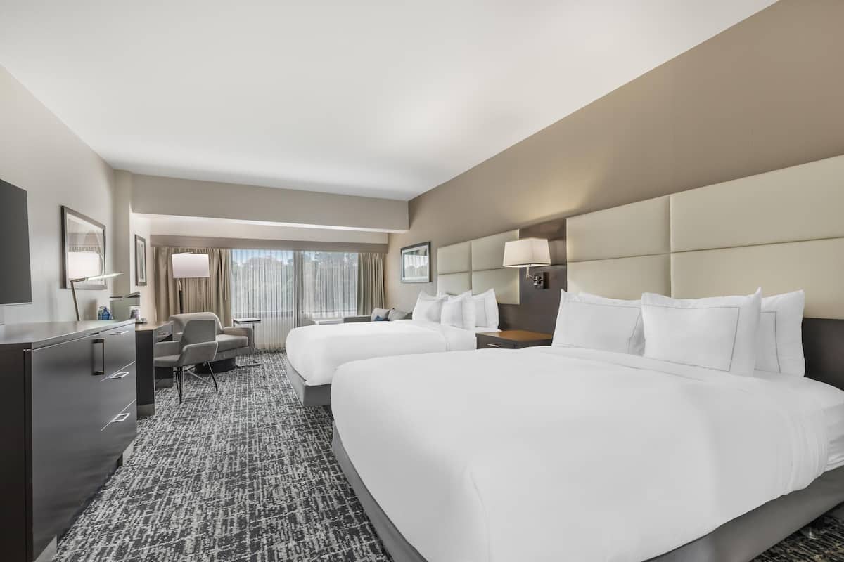 A hotel room with two beds, a desk, a chair, a TV, and a window with curtains.
