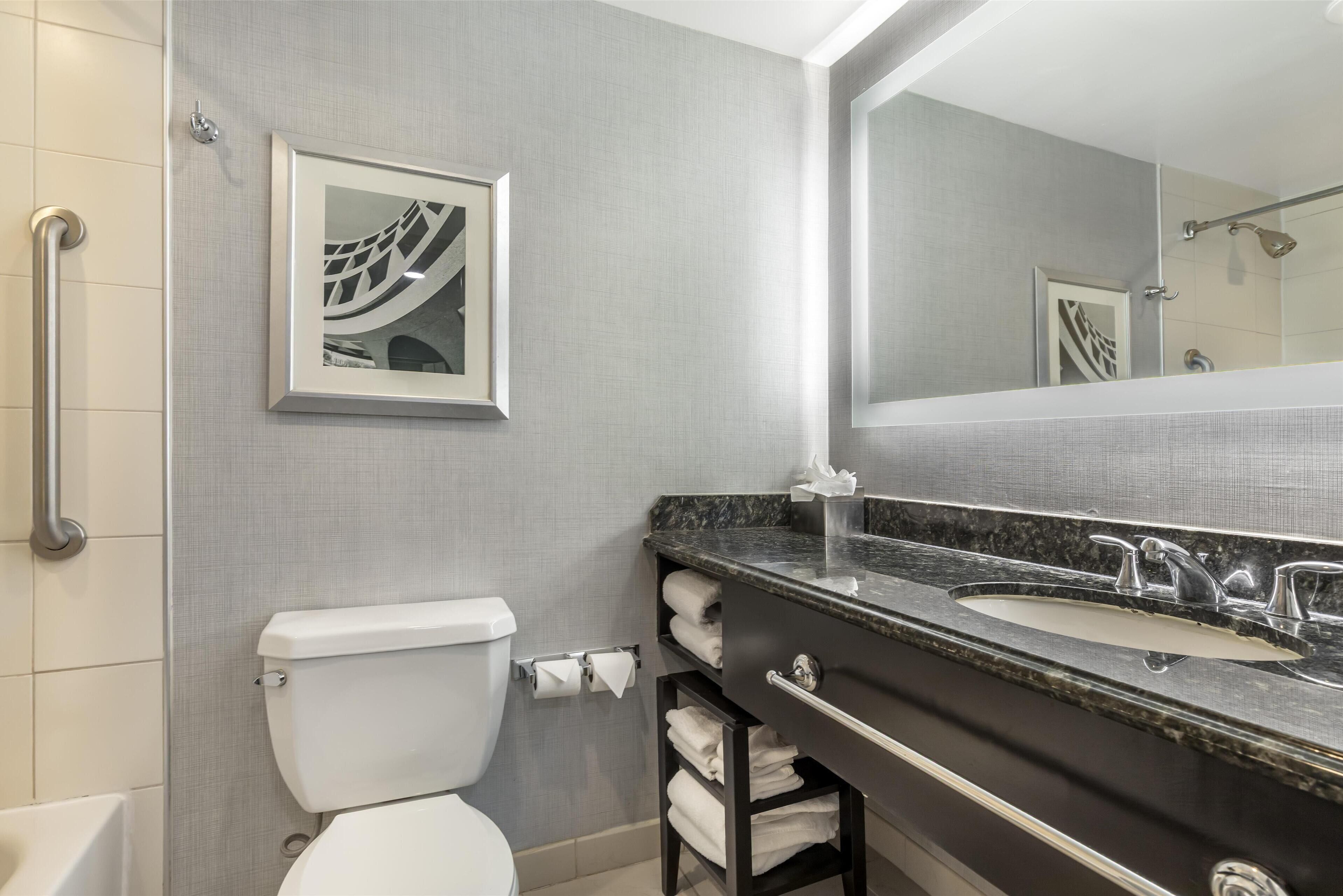 A modern bathroom with a toilet, a sink, a mirror, and a shower area.
