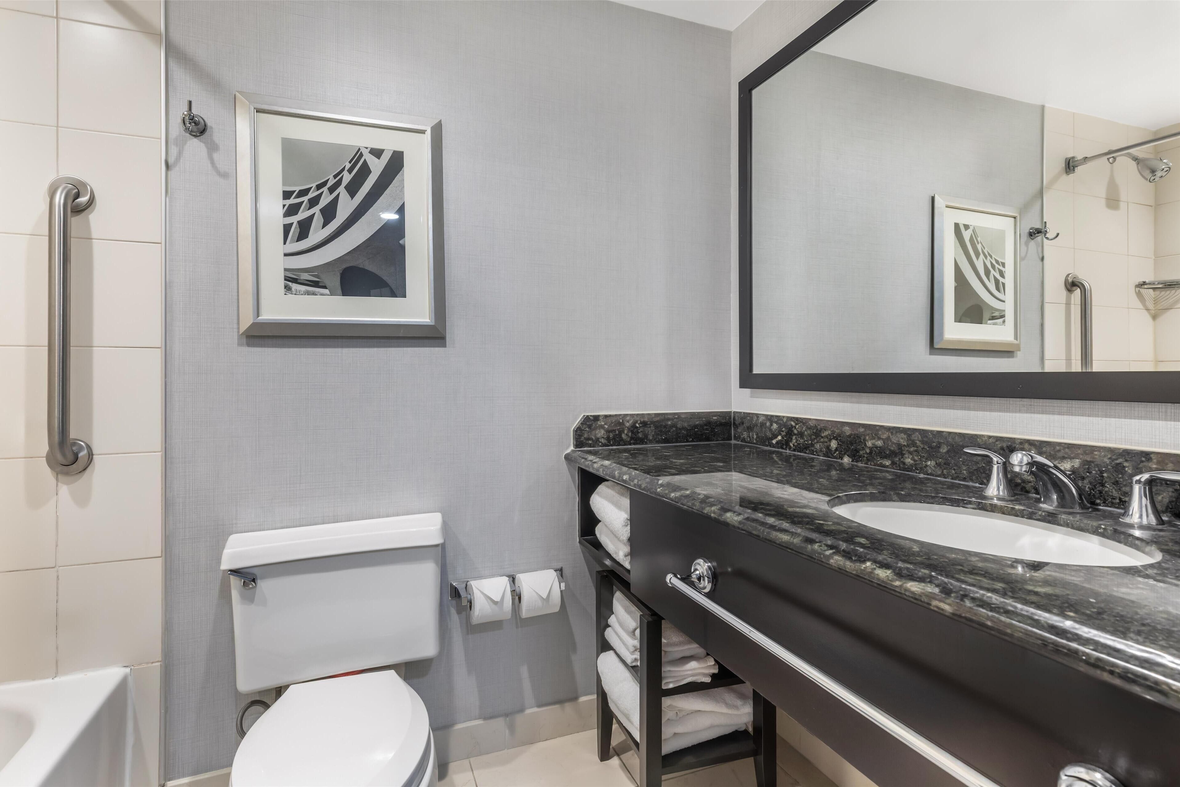 Une salle de bain moderne avec des toilettes blanches, un grand miroir, un lavabo en marbre noir et un espace douche.