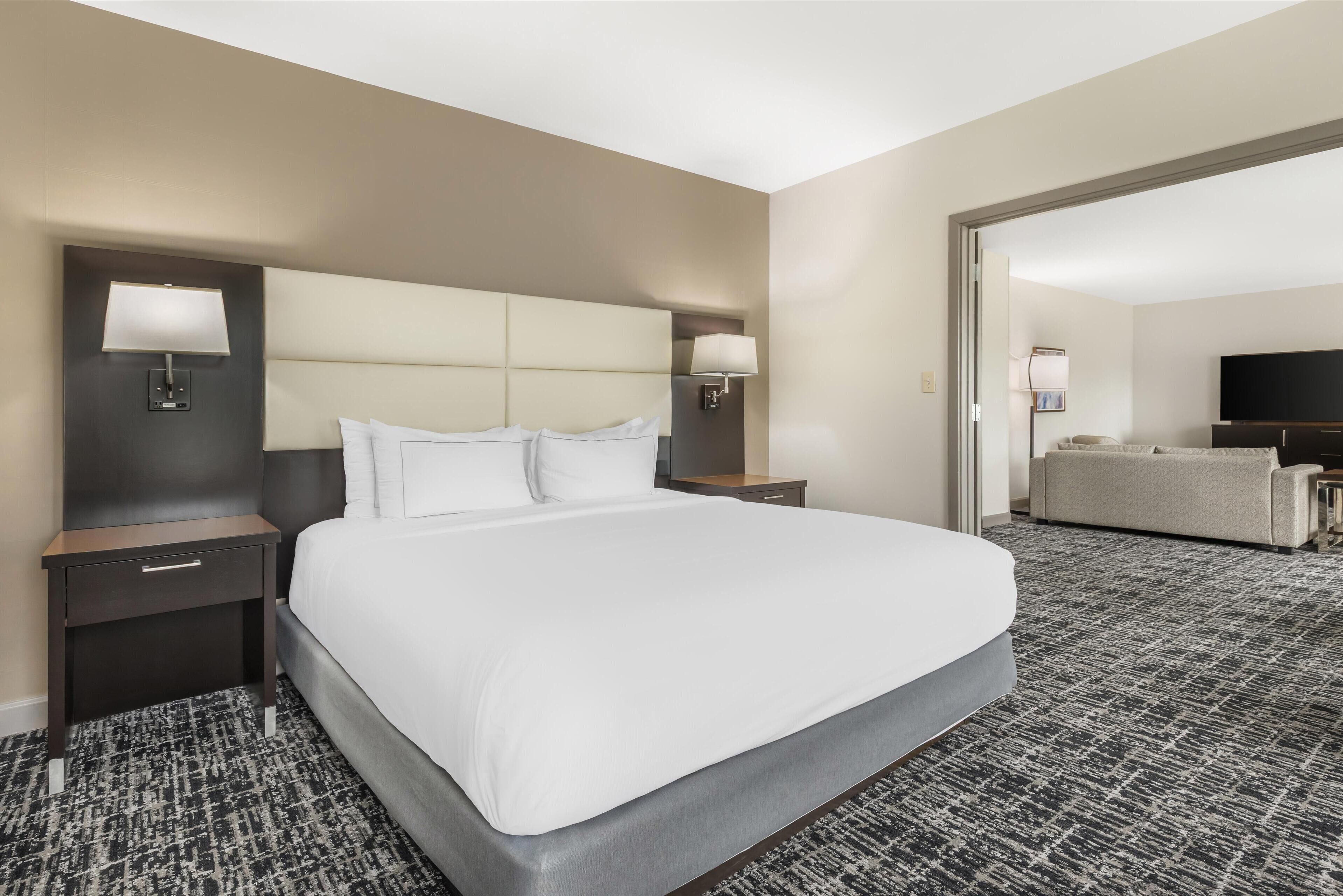 Une chambre d’hôtel dotée d’un grand lit, de deux tables de chevet avec lampes, d’un téléviseur à écran plat et d’un canapé dans l’espace salon attenant.
