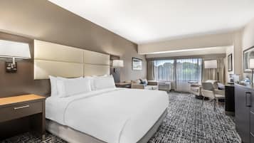 A hotel room with a large bed, a desk, a chair, a sofa, and a view of the city through the window.