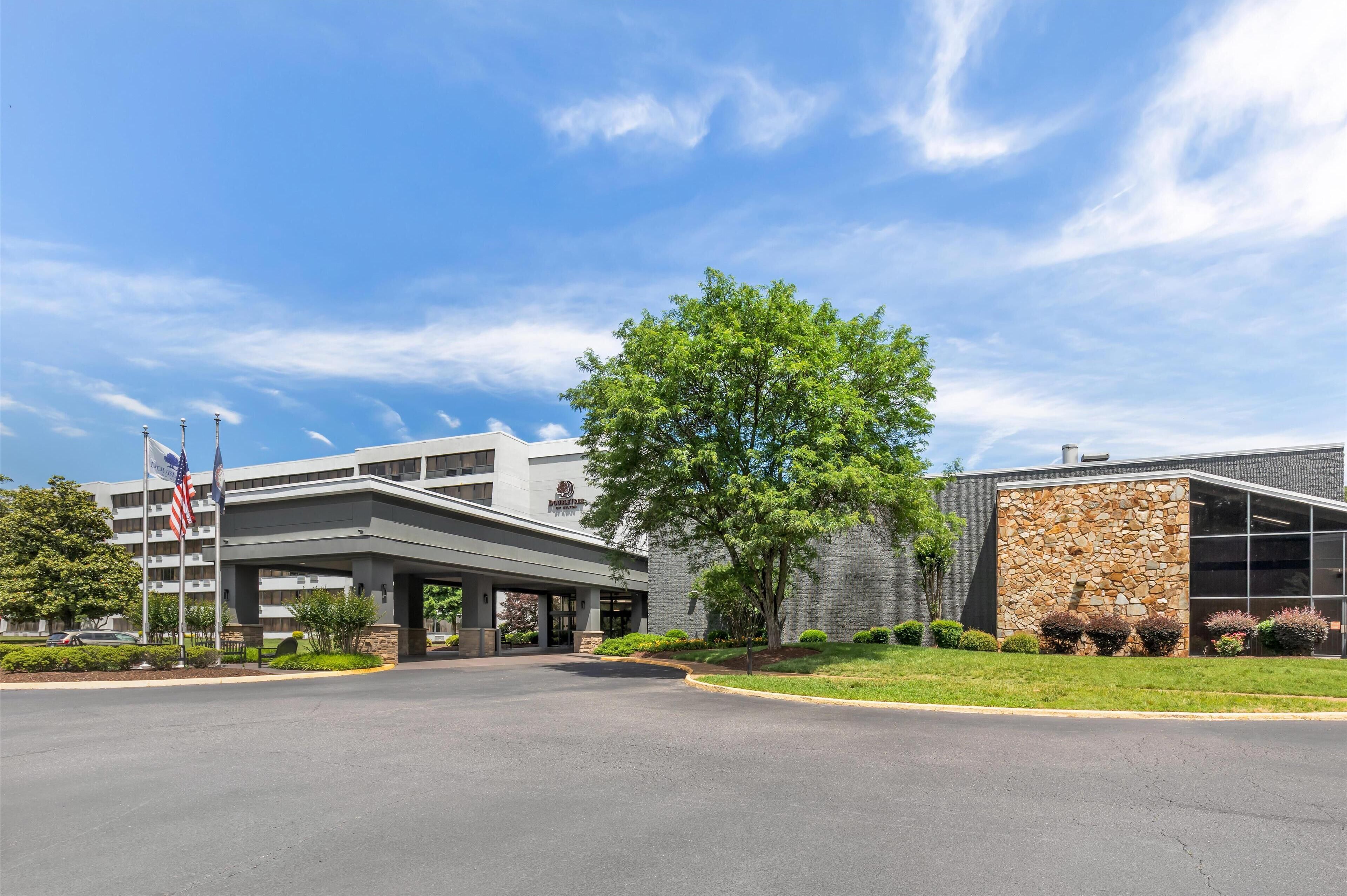 A hotel entrance with a covered walkway, stone facade, and landscaped greenery.