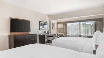 A hotel room with two beds, a desk, a television, and a large window with curtains.