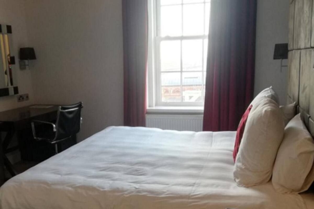 A hotel room with a bed, a desk, a chair, a window with curtains, and a view of the outside.