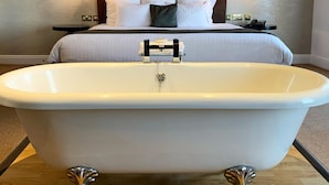 Une chambre dotée d’une grande baignoire, d’un lit avec du linge de lit blanc et d’une tête de lit sombre.
