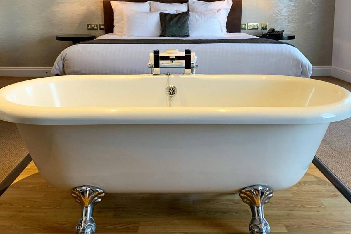 A room with a large bathtub, a bed with white linens, and a dark headboard.