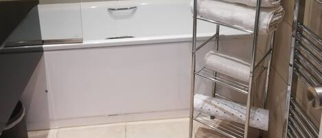 A bathroom with a white bathtub, a towel rack with folded towels, and a black trash bin.