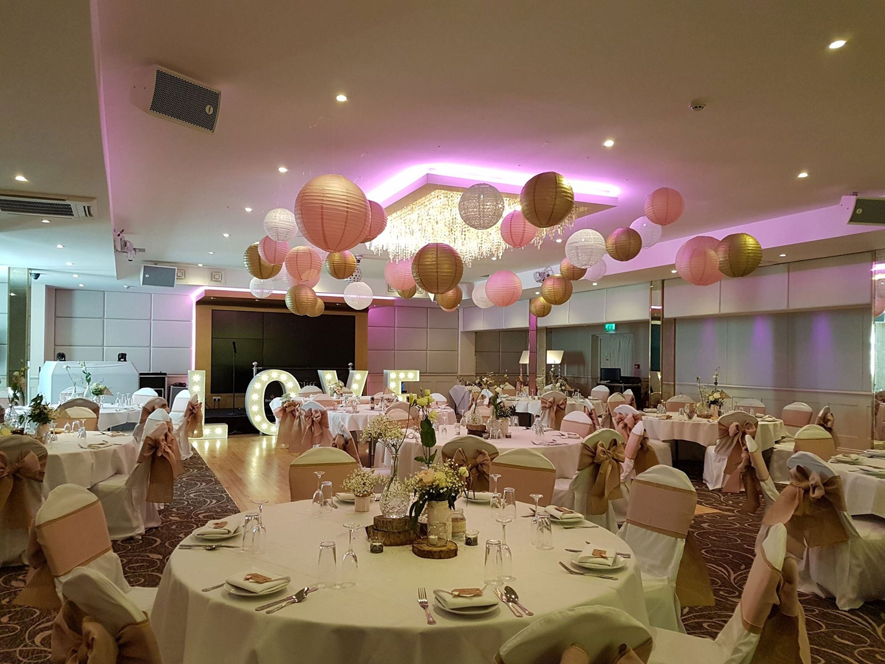 Un salón de banquetes con mesas redondas, manteles blancos y fajas doradas.