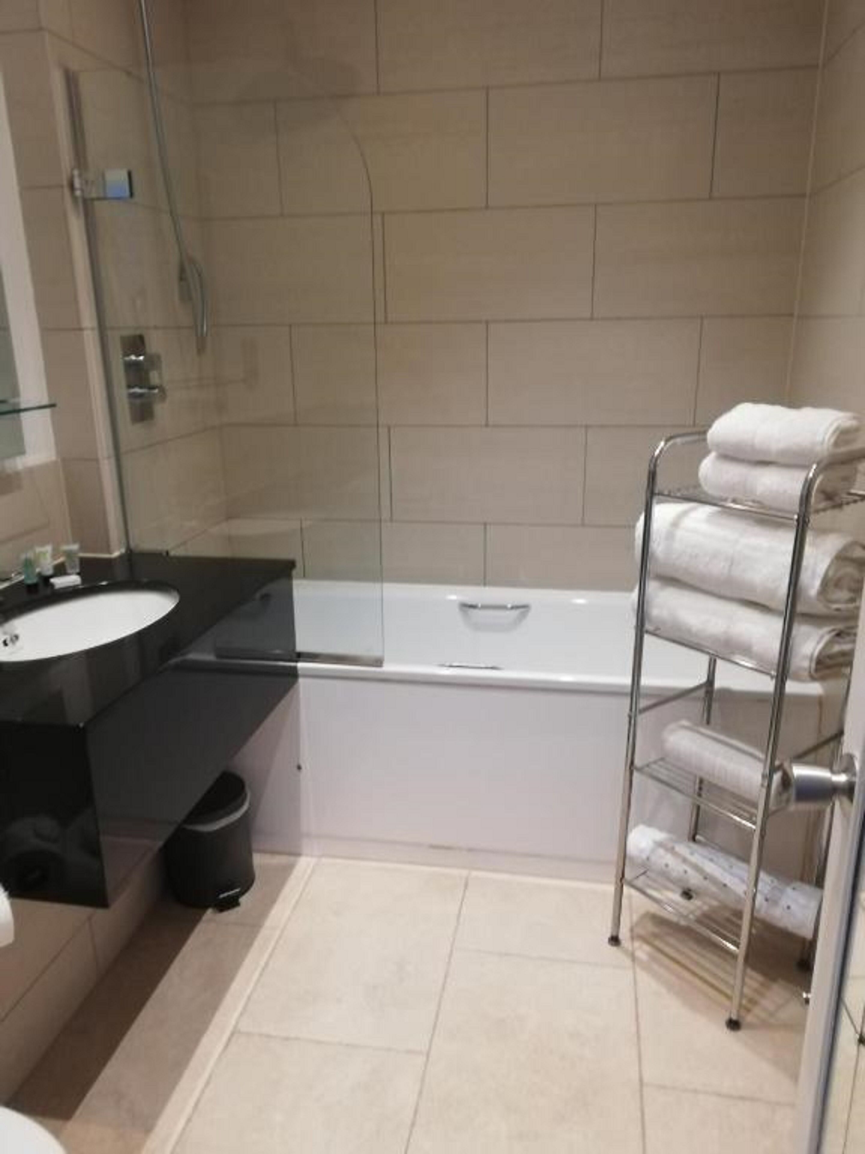 Een moderne badkamer met een badkuip, een glazen douchecabine, een zwart aanrecht met een wastafel en een handdoekrek met opgevouwen handdoeken.